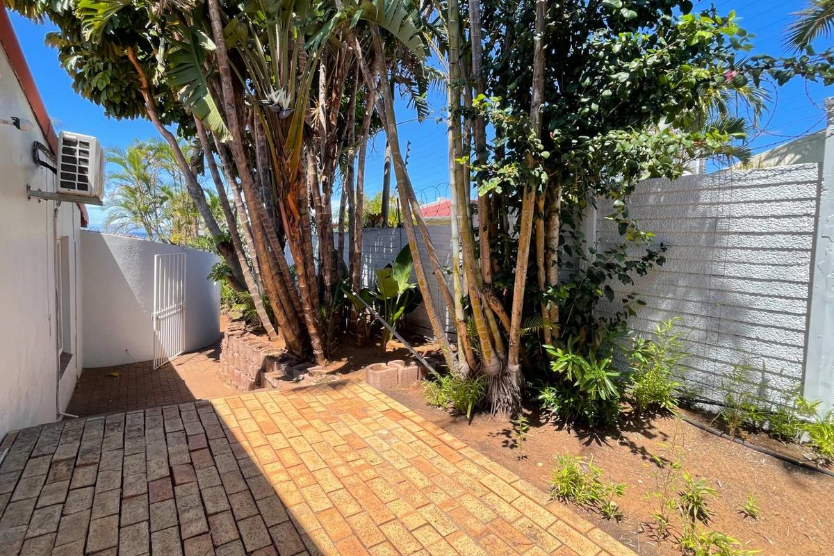 A private rear courtyard featuring brick paving, established trees, and a secure boundary wall with an external air conditioning unit.