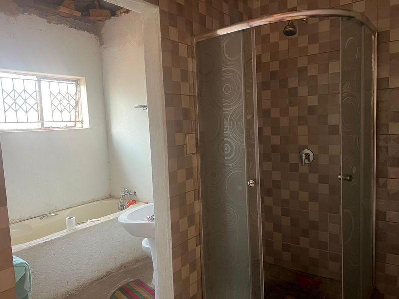 A bathroom featuring a shower enclosure, bathtub, and pedestal basin, currently requiring renovation and finishing of the ceiling and wall areas.