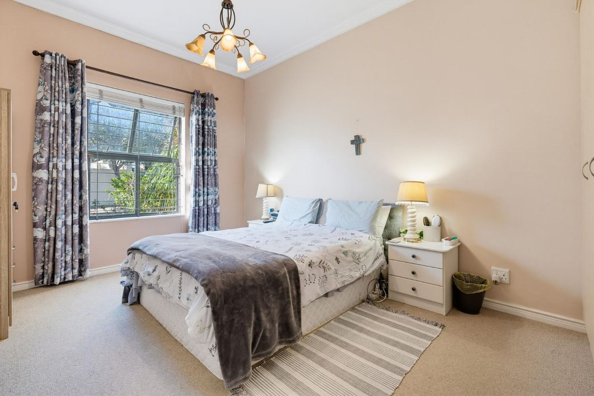 A well-lit bedroom featuring carpeted flooring, built-in wardrobe storage, and a window fitted with security bars.