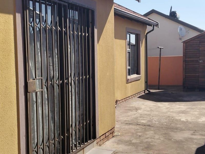 Rear exterior view of the property featuring a concrete paved area, security gate, and boundary wall.