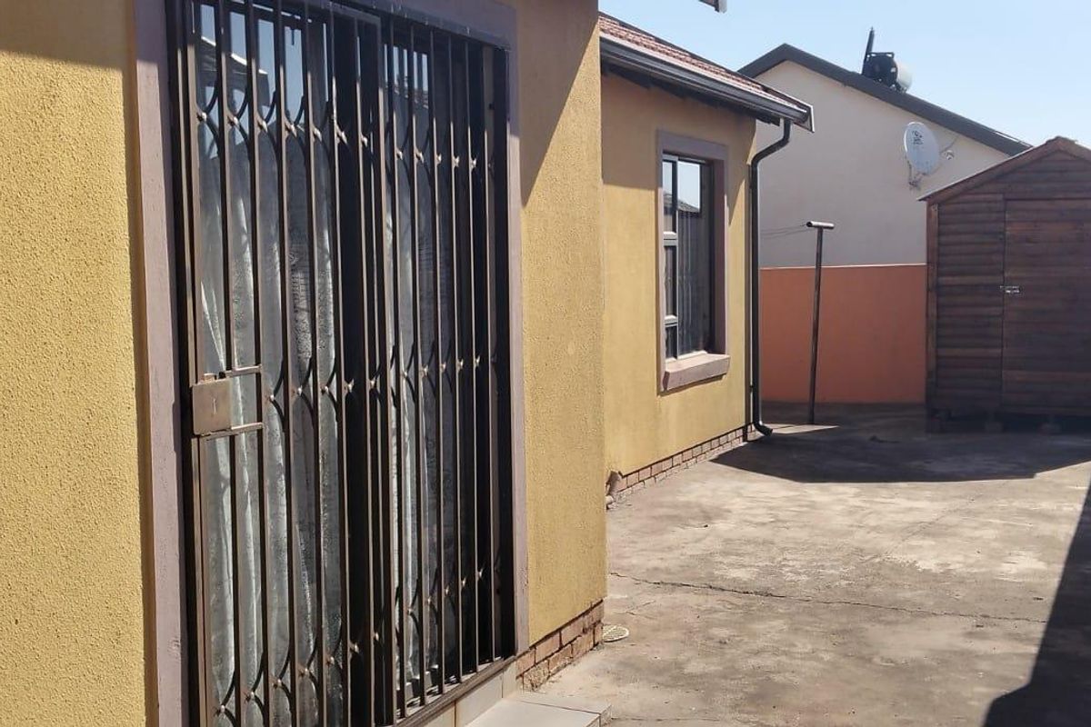 Rear exterior view of the property featuring a concrete paved area, security gate, and boundary wall.