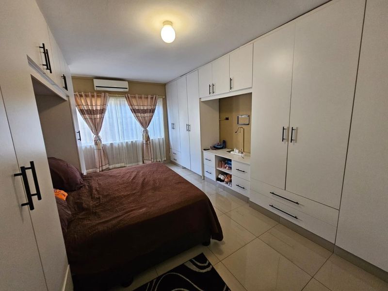A well-maintained bedroom featuring extensive white built-in cabinetry, tiled flooring, and a wall-mounted air conditioning unit.