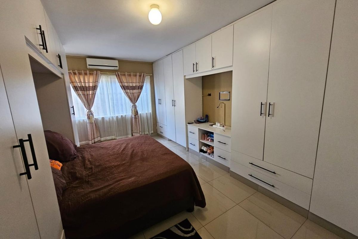 A well-maintained bedroom featuring extensive white built-in cabinetry, tiled flooring, and a wall-mounted air conditioning unit.