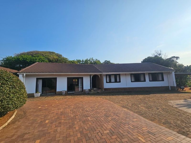 A well-maintained single-story residential home featuring a tiled roof, brick-paved driveway, and a classic facade with sliding glass doors and an arched entrance.