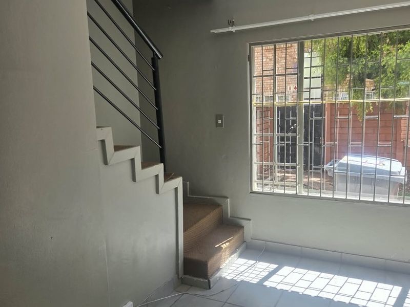 An empty living area featuring tiled floors, a staircase with a metal balustrade, and a window fitted with security bars.