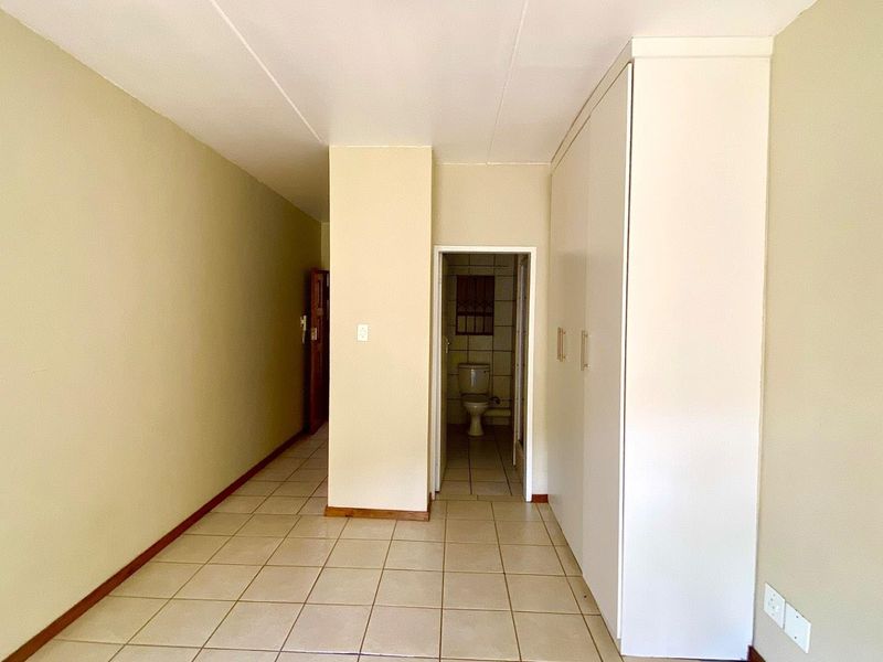 An empty bedroom featuring tiled flooring, built-in cupboards, and direct access to an en-suite bathroom.