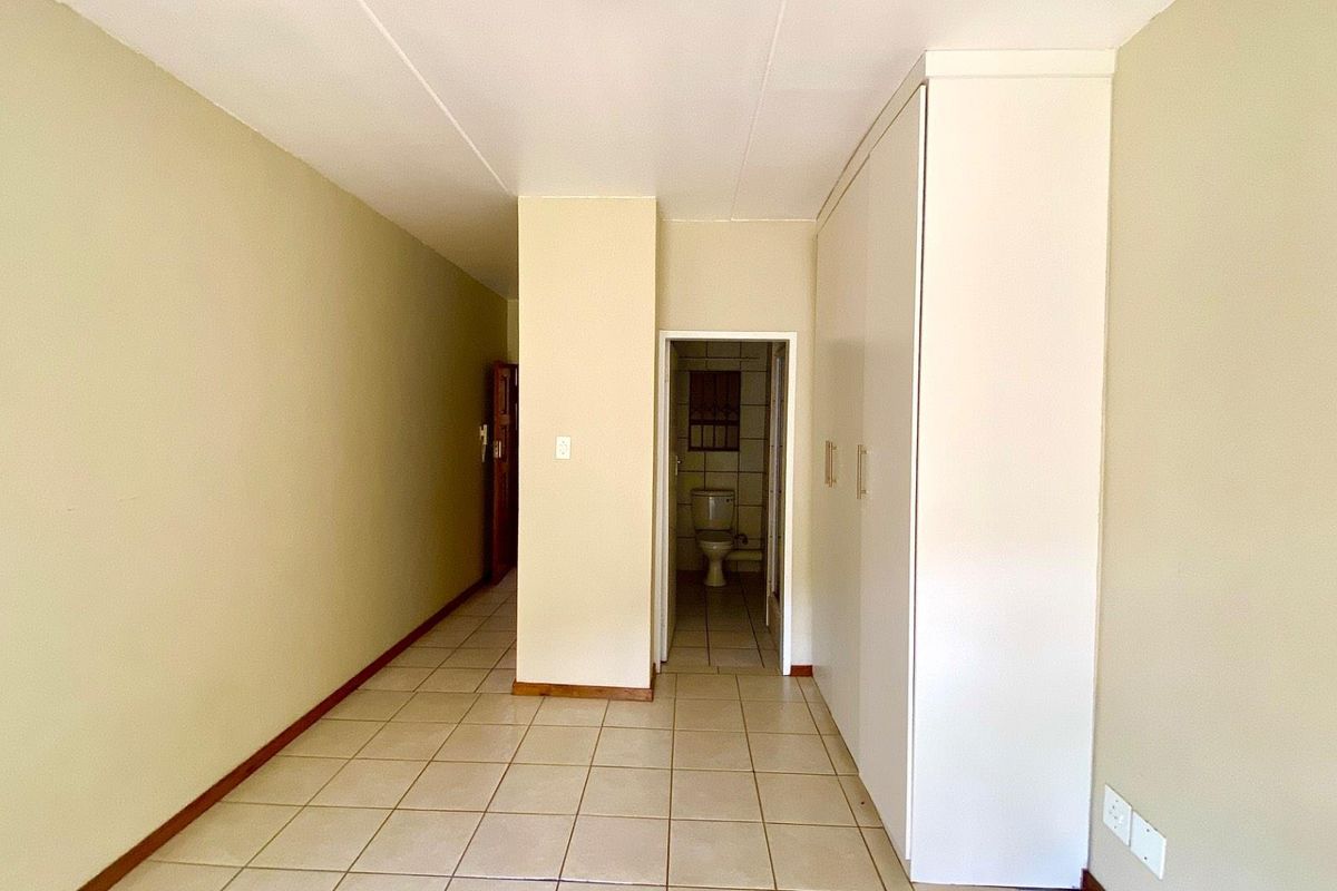 An empty bedroom featuring tiled flooring, built-in cupboards, and direct access to an en-suite bathroom.