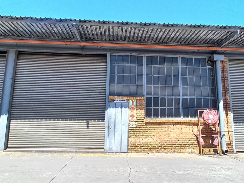 Industrial warehouse exterior featuring multiple roller shutter doors, face brick facade, steel window frames, and a concrete apron.