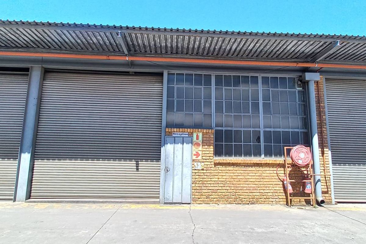 Industrial warehouse exterior featuring multiple roller shutter doors, face brick facade, steel window frames, and a concrete apron.