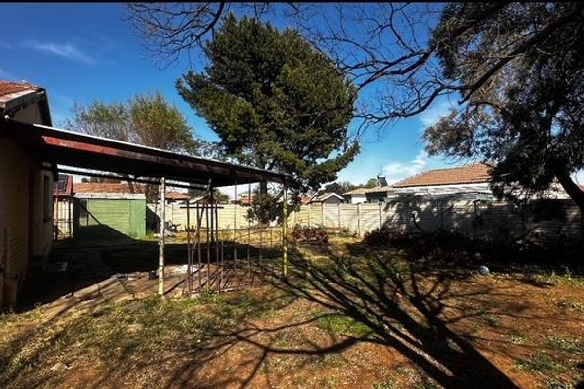 Rear garden area featuring a covered patio structure, perimeter precast concrete walling, and mature trees.