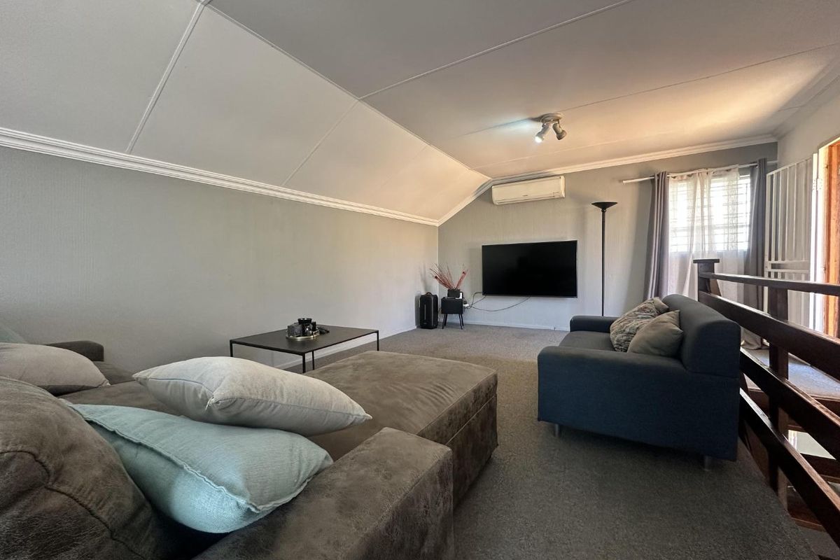 A spacious loft-style living area featuring a raked ceiling, wall-mounted air conditioning unit, and carpeted flooring.