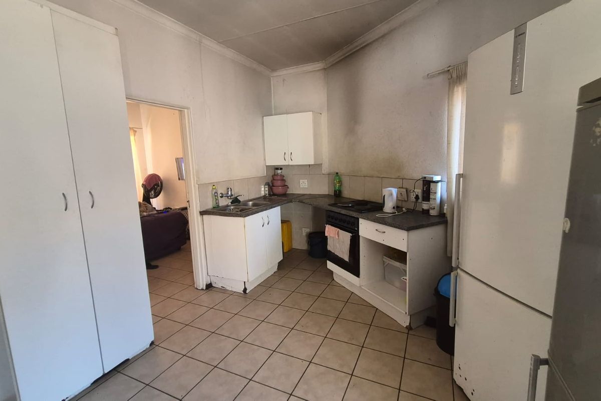 A functional kitchen featuring tiled flooring, built-in cabinetry, and a freestanding stove, requiring cosmetic updates to improve its overall condition and aesthetic appeal.