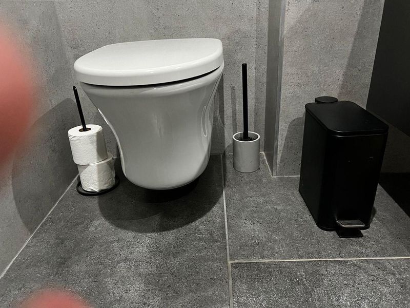 A modern bathroom featuring a wall-mounted toilet with contemporary grey stone-look floor and wall tiling.
