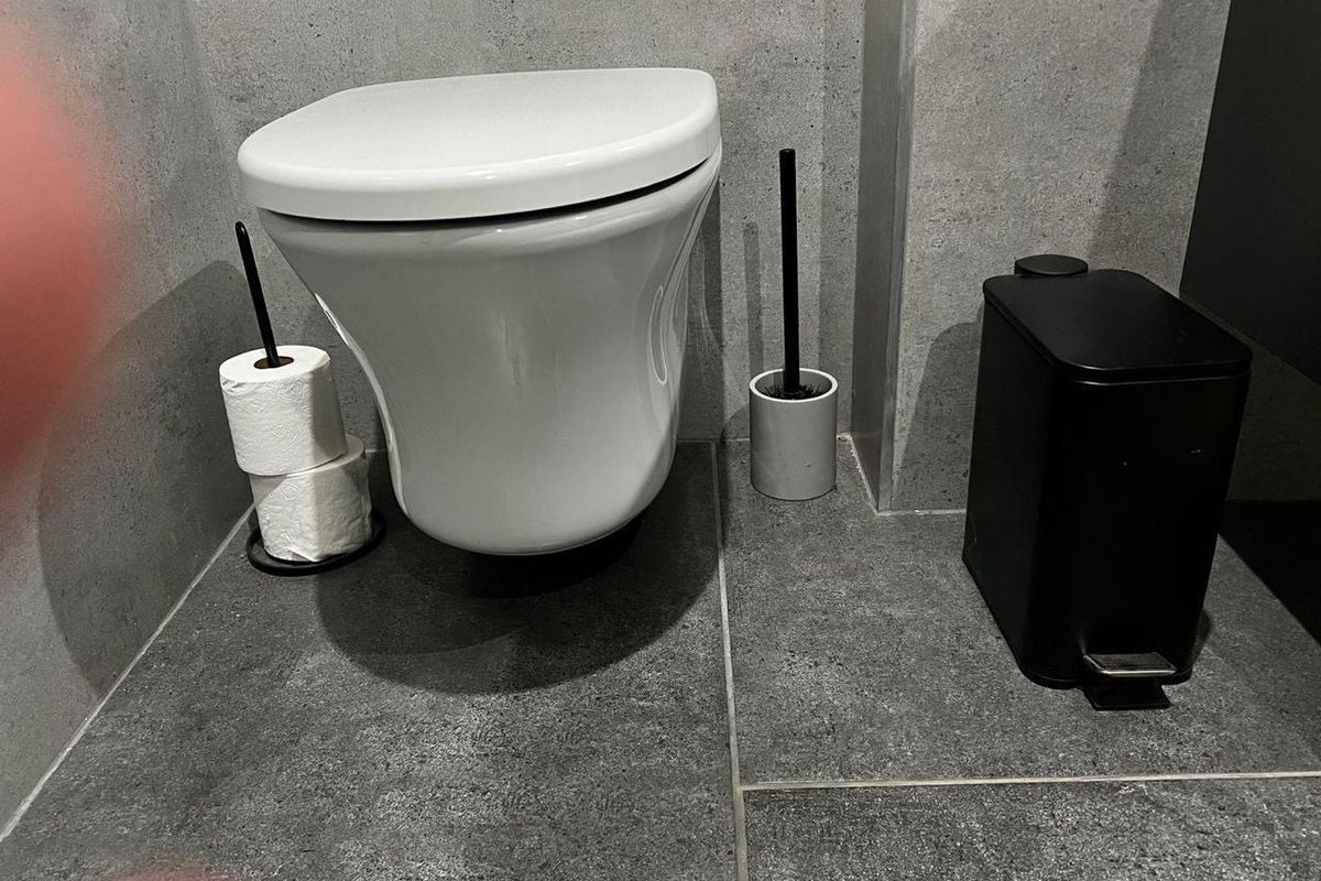 A modern bathroom featuring a wall-mounted toilet with contemporary grey stone-look floor and wall tiling.