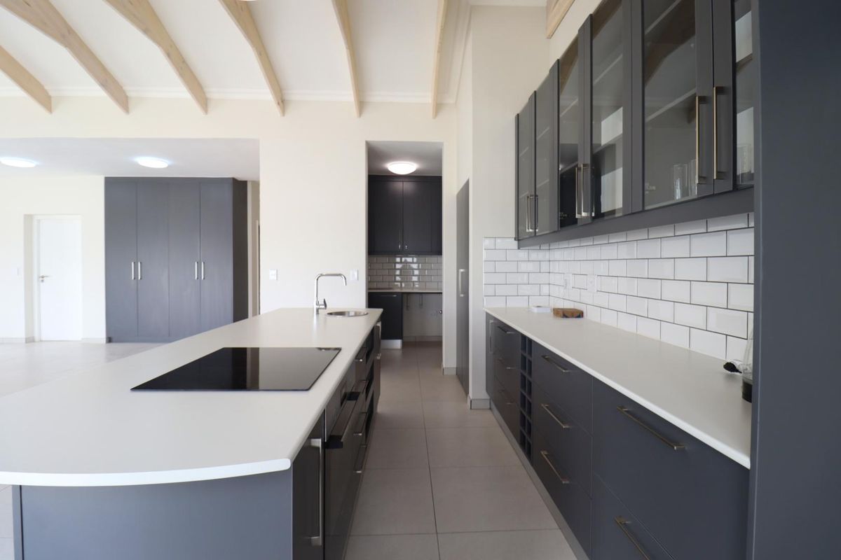Modern kitchen featuring a large island with induction cooktop, sleek dark cabinetry, subway tile backsplash, and exposed timber ceiling beams.