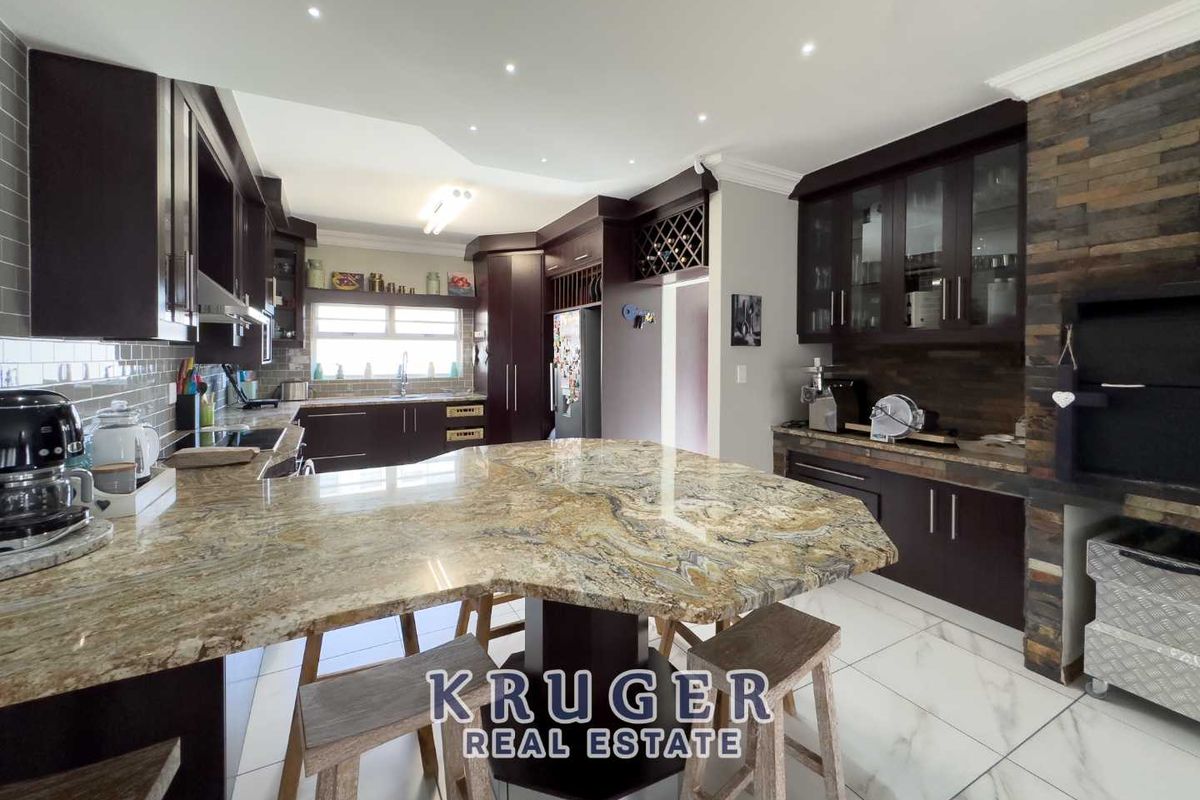 Spacious kitchen featuring dark cabinetry, granite countertops, a large central island, and a built-in indoor braai area with stone cladding.