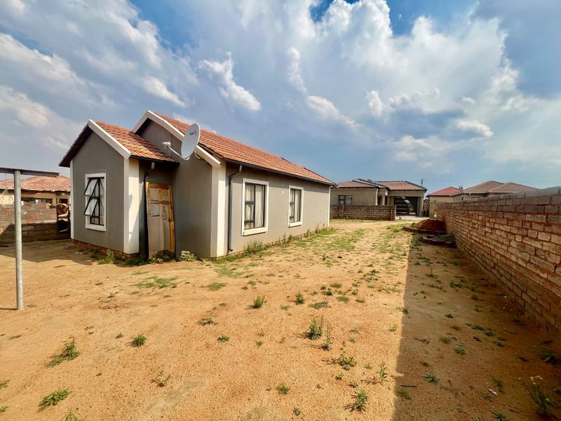 Rear view of a detached house featuring a tiled roof, casement windows, and a large, unlandscaped sandy yard enclosed by a brick boundary wall.
