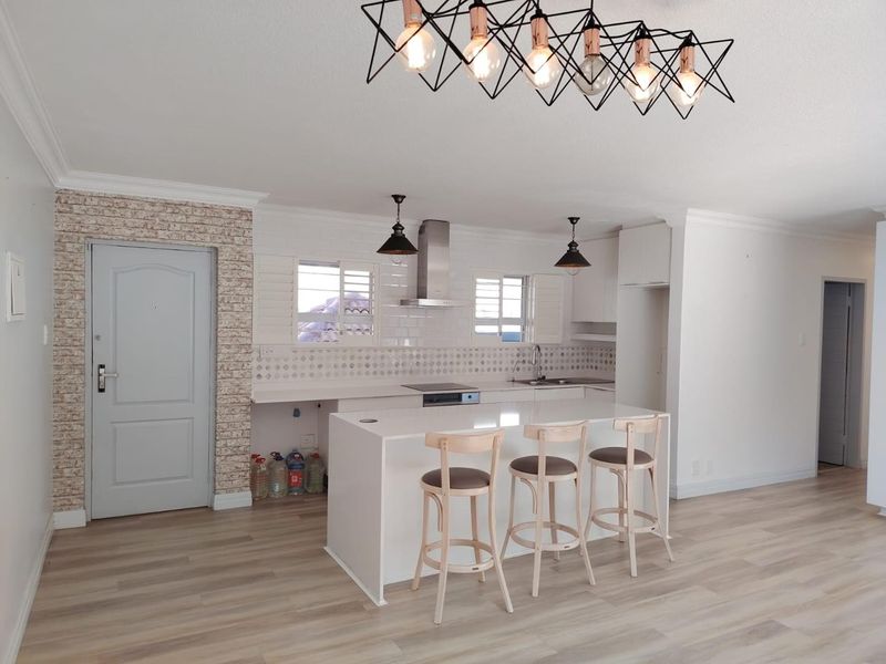 Modern open-plan kitchen featuring a central island, sleek cabinetry, integrated cooktop, extractor fan, and stylish light fixtures, complemented by light laminate flooring.