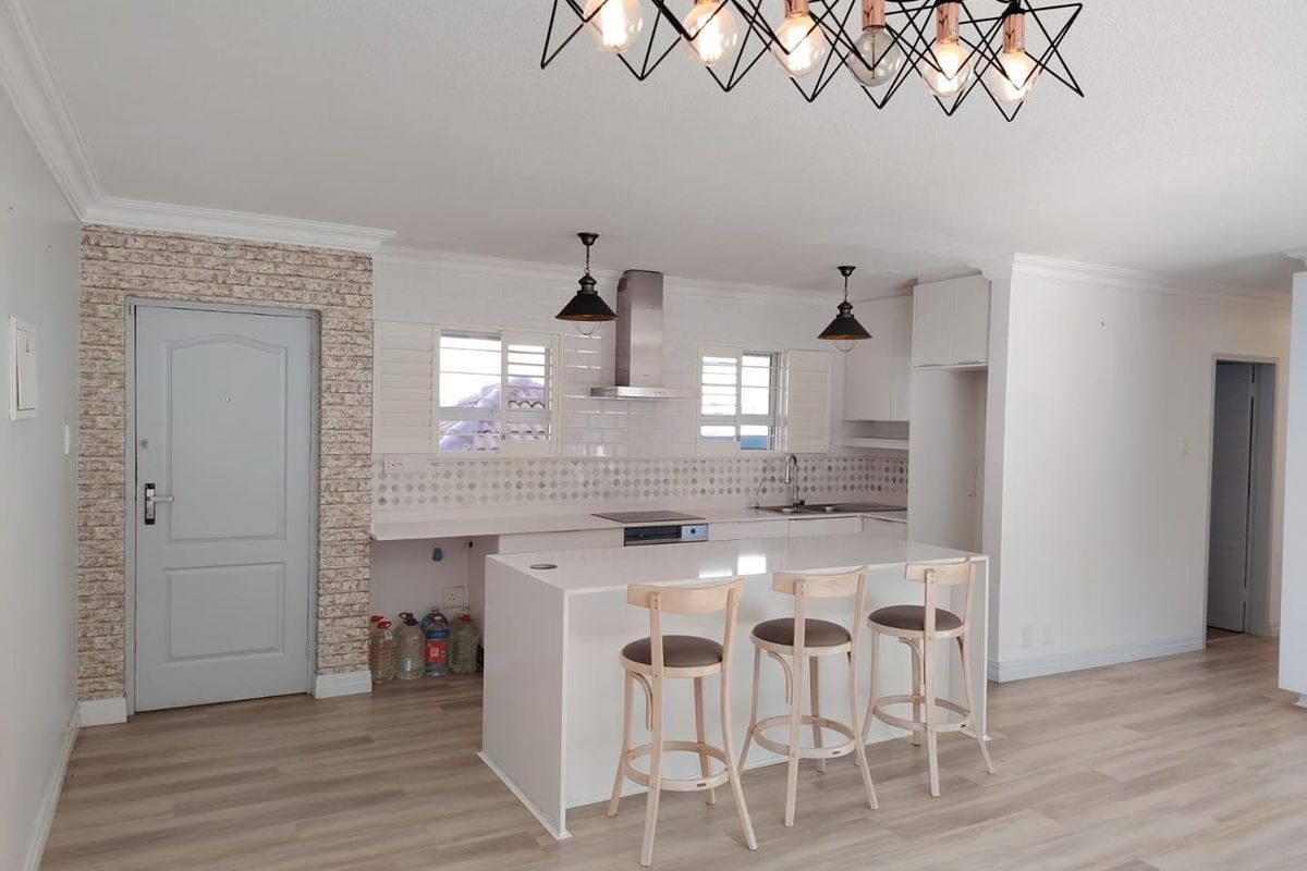 Modern open-plan kitchen featuring a central island, sleek cabinetry, integrated cooktop, extractor fan, and stylish light fixtures, complemented by light laminate flooring.