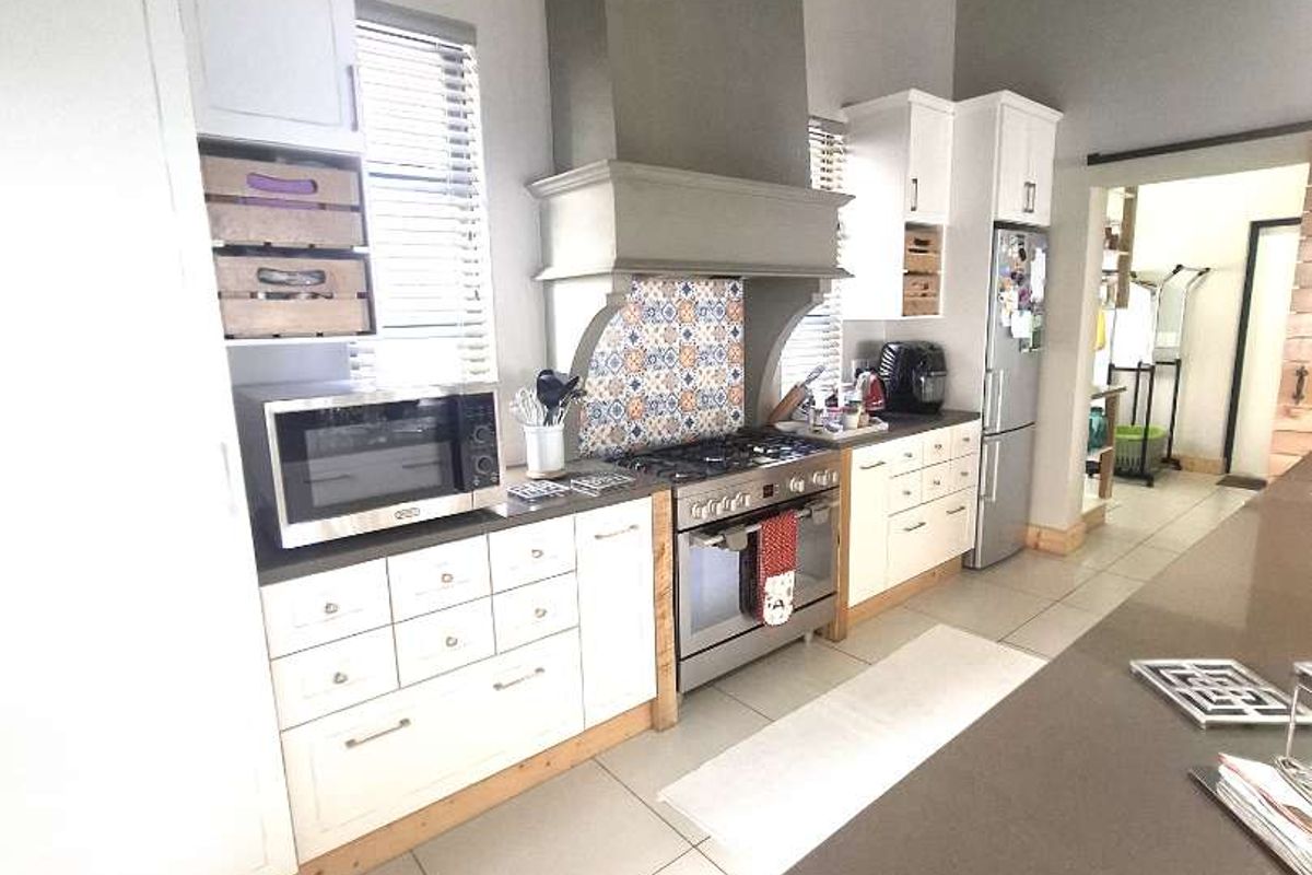 A modern kitchen featuring white cabinetry, a gas stove with a decorative tiled backsplash, a large extractor hood, and a spacious island with stone countertops.