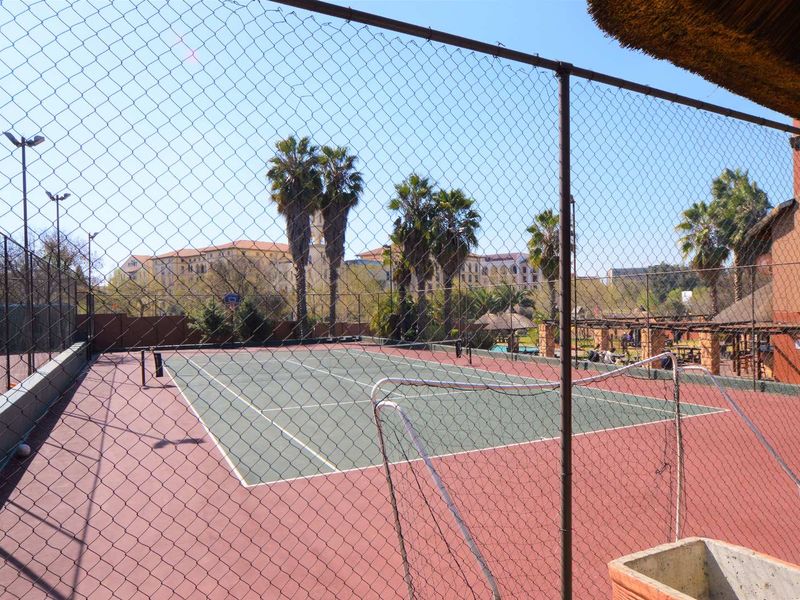 A well-maintained outdoor tennis court facility enclosed by chain-link fencing, featuring floodlights and a hard-surface court.