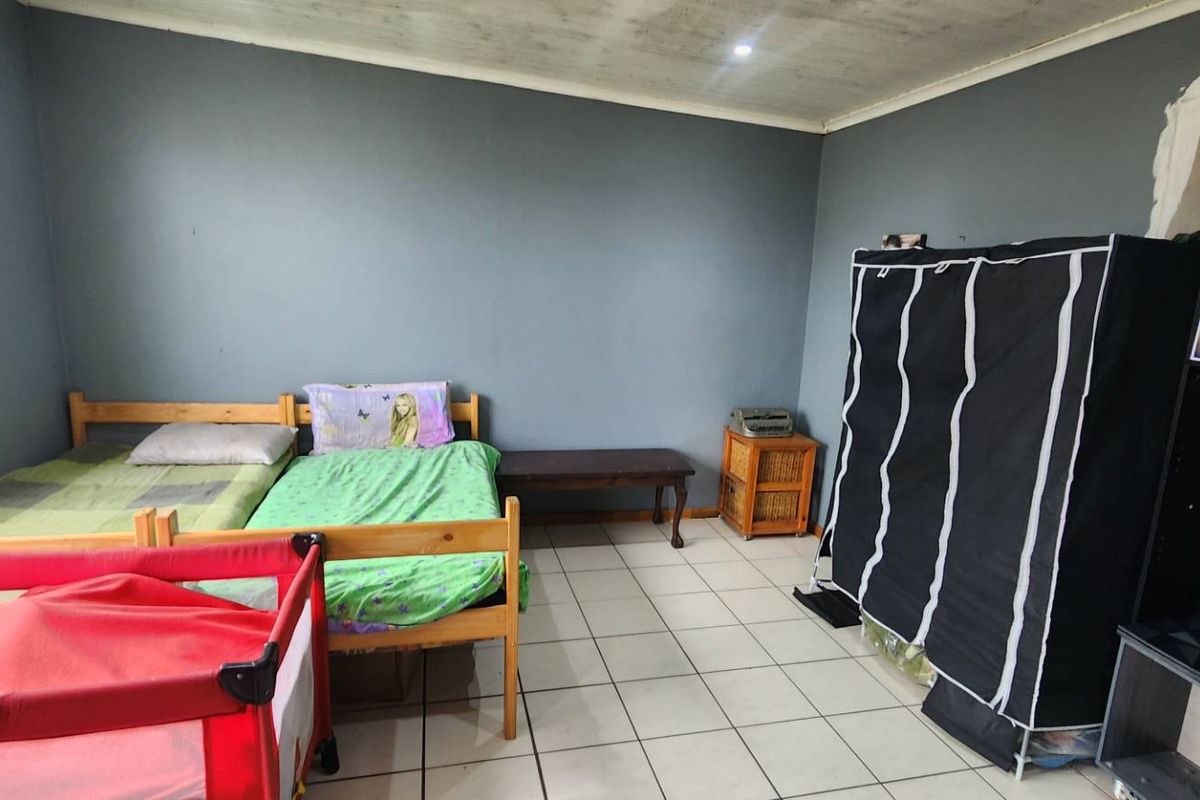 A bedroom featuring tiled flooring and security bars on the window, currently requiring minor cosmetic repairs to the wall plastering and paintwork.
