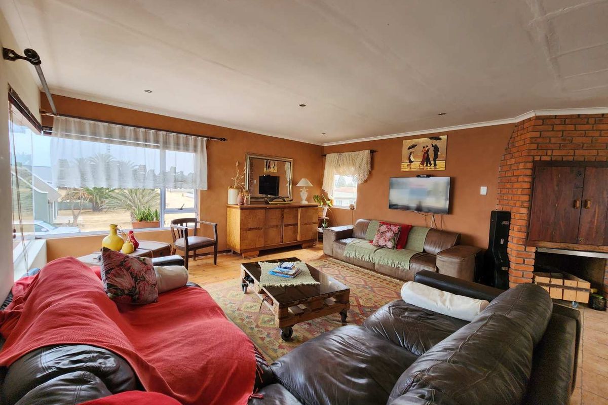 Spacious living room featuring a prominent face-brick fireplace, large windows providing natural light, and wooden flooring.