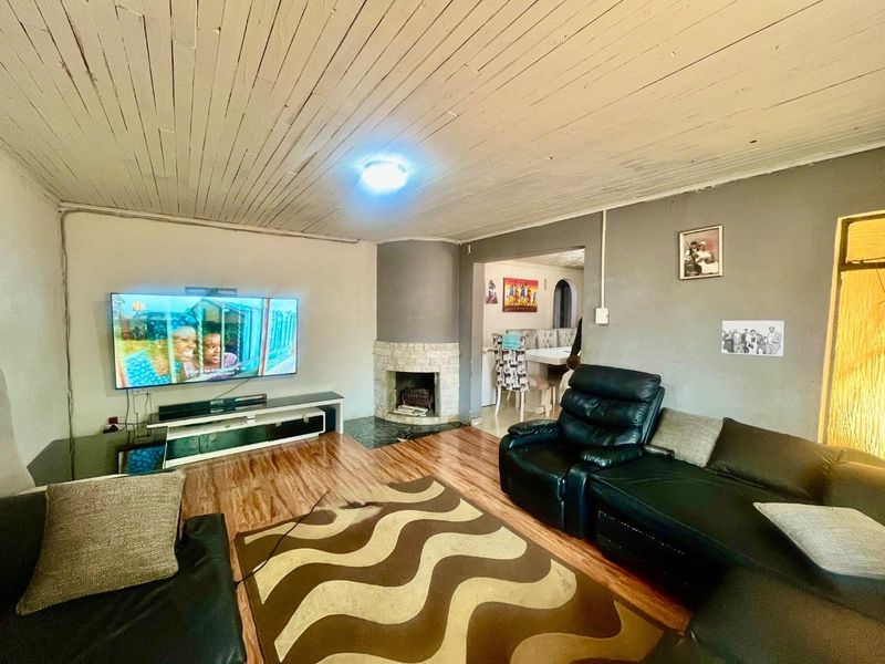 A living room featuring a stone-clad fireplace, laminate flooring, and a timber-slat ceiling, with an open-plan flow into the adjacent dining area.