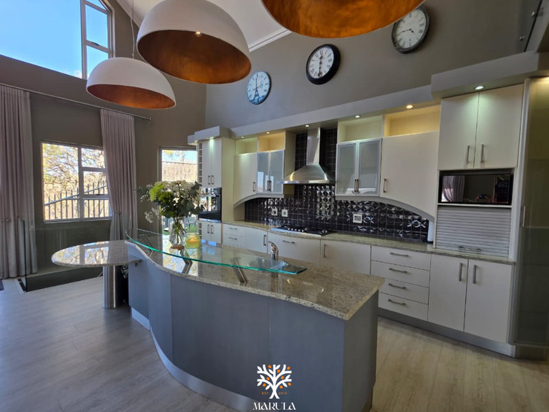 Modern kitchen featuring granite countertops, a curved breakfast bar, built-in appliances, and high ceilings with ample natural light.