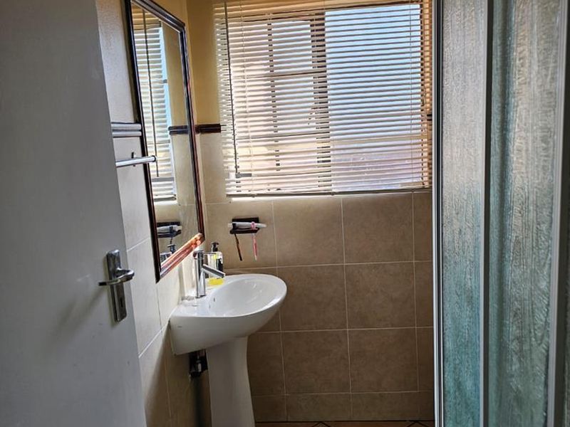 A functional bathroom featuring a pedestal basin, tiled walls and flooring, and a shower enclosure with a window for natural light.