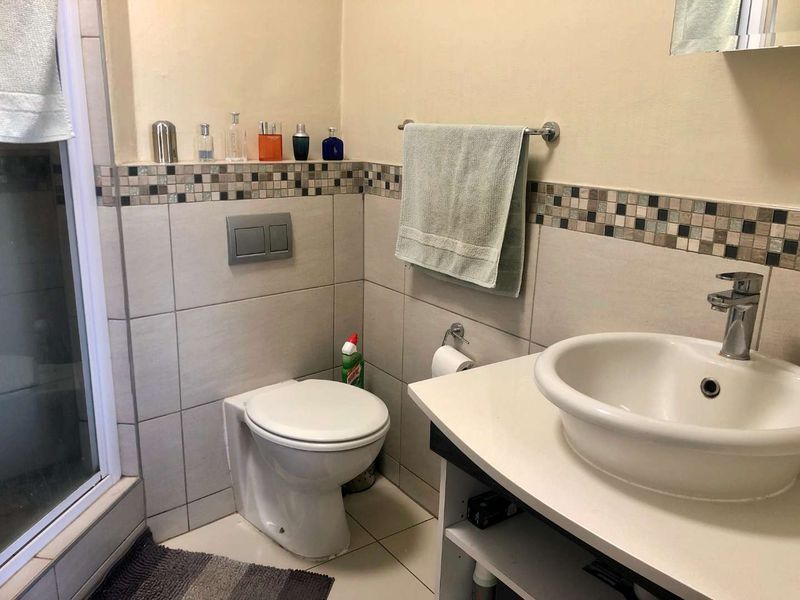 A functional bathroom featuring a wall-mounted toilet, vessel sink with chrome faucet, shower enclosure, and decorative mosaic tile accents.