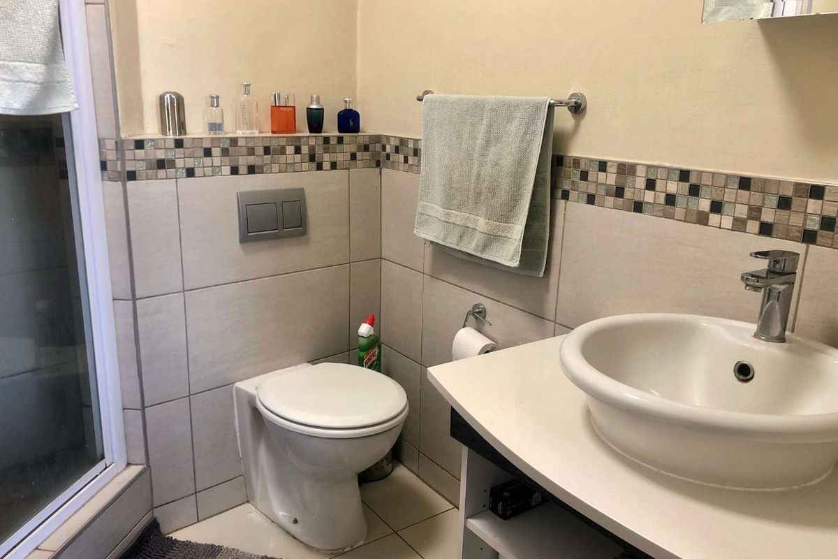 A functional bathroom featuring a wall-mounted toilet, vessel sink with chrome faucet, shower enclosure, and decorative mosaic tile accents.