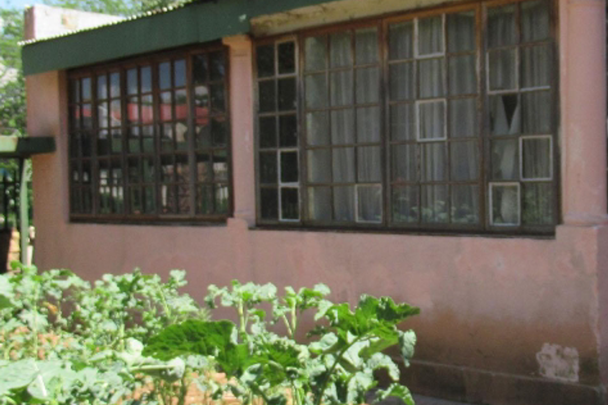 Exterior view of a residential building featuring aged masonry walls, timber-framed windows, and a corrugated metal roof, set alongside a garden area.
