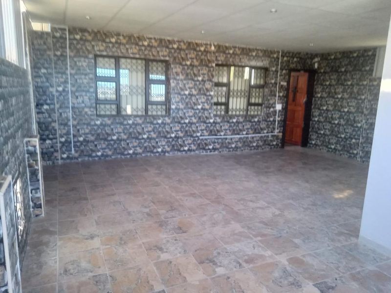 An empty, spacious living area featuring tiled flooring, patterned wall finishes, and secure window treatments, offering a blank canvas for interior design.