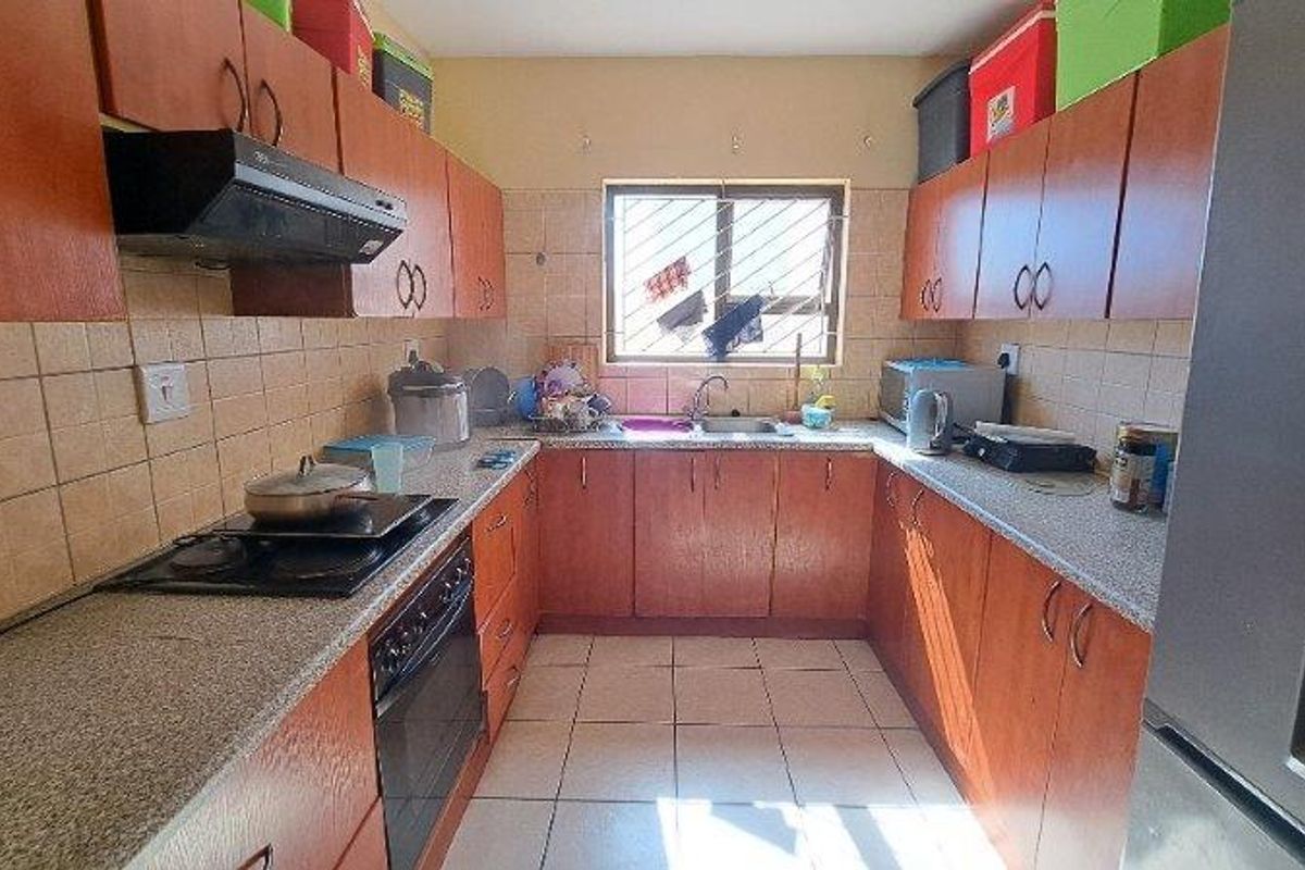 A functional U-shaped kitchen featuring wood-tone cabinetry, tiled splashbacks, built-in oven, hob, and extractor fan with a central window.