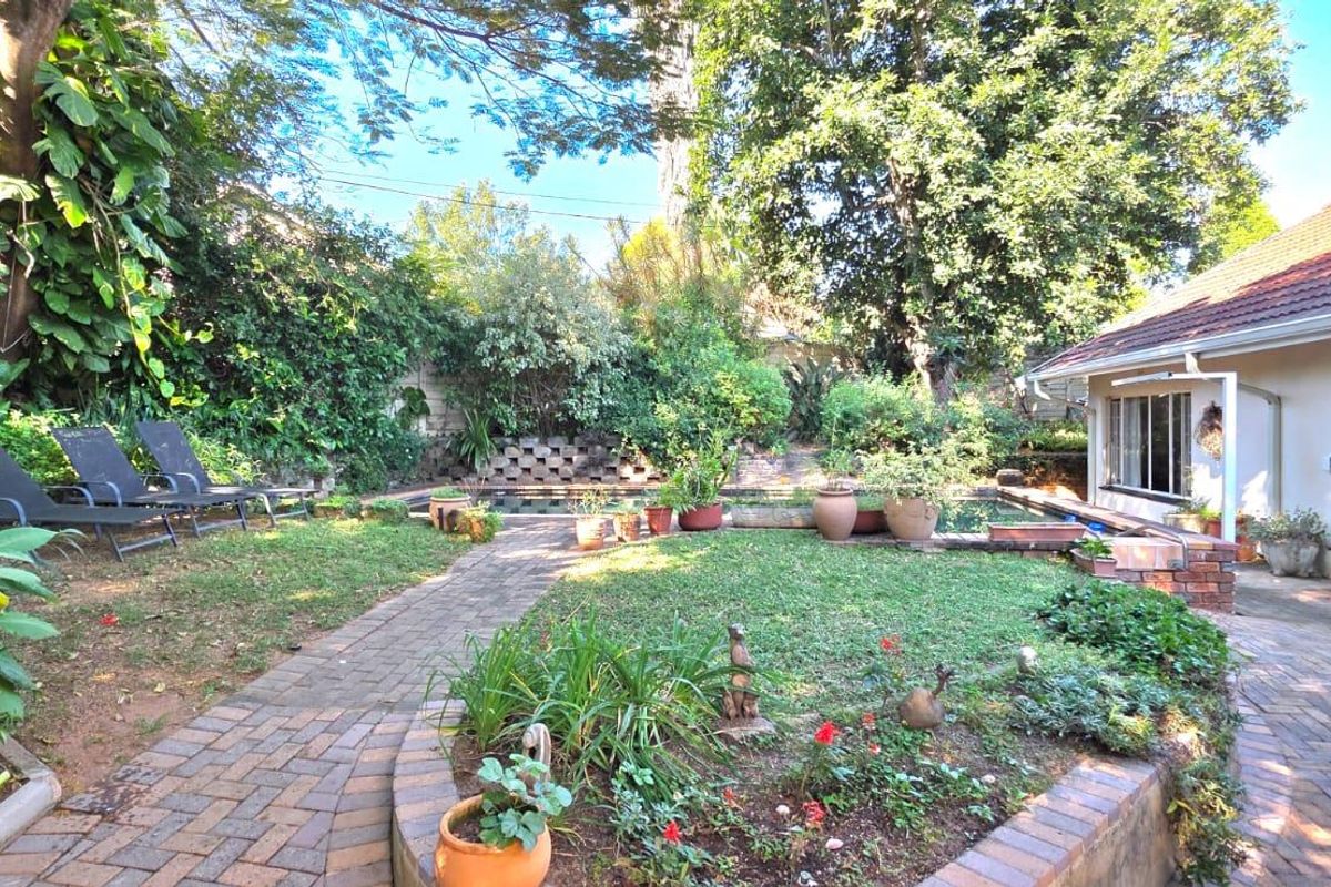 A private rear garden featuring a swimming pool, paved walkways, established landscaping, and direct access to the home via sliding glass doors.