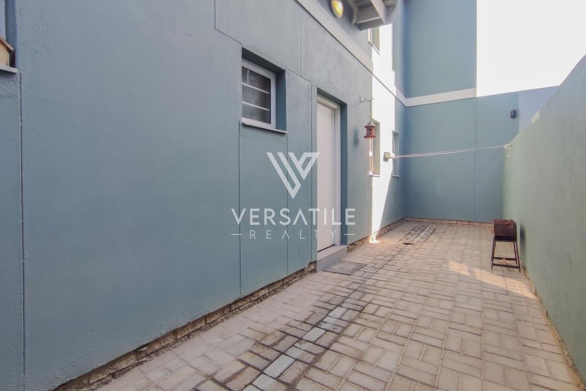 A paved rear courtyard area featuring a solid boundary wall, exterior lighting, and a utility door access point.
