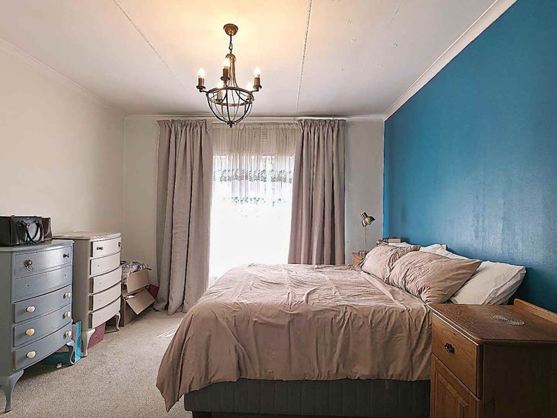 A bedroom featuring carpeted flooring, a central chandelier, and a blue accent wall, with visible signs of wear on the ceiling.