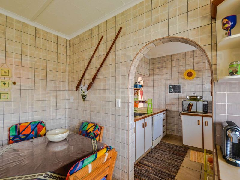 A dated kitchen featuring full-height wall tiling, an arched entryway, and functional built-in cabinetry with a separate prep or wash-up area.