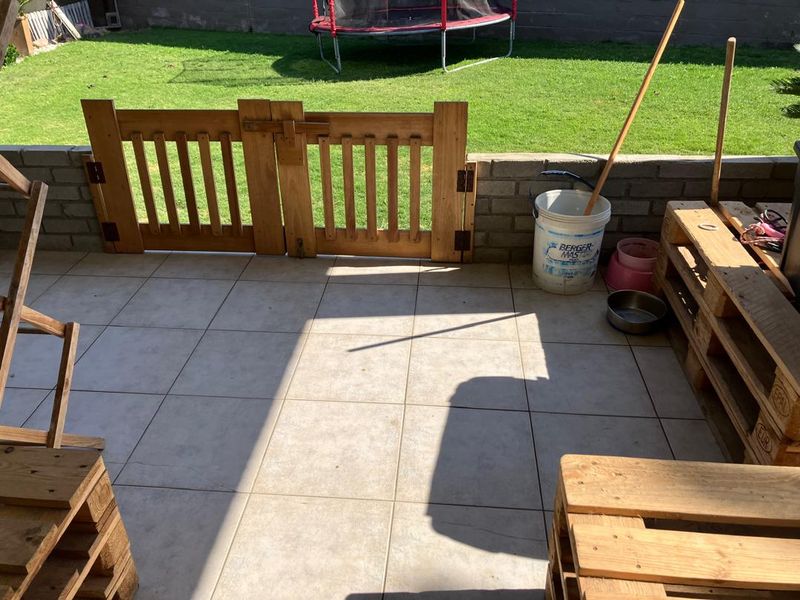 A covered patio area featuring tiled flooring, a low brick retaining wall, and a wooden safety gate leading to the rear garden.