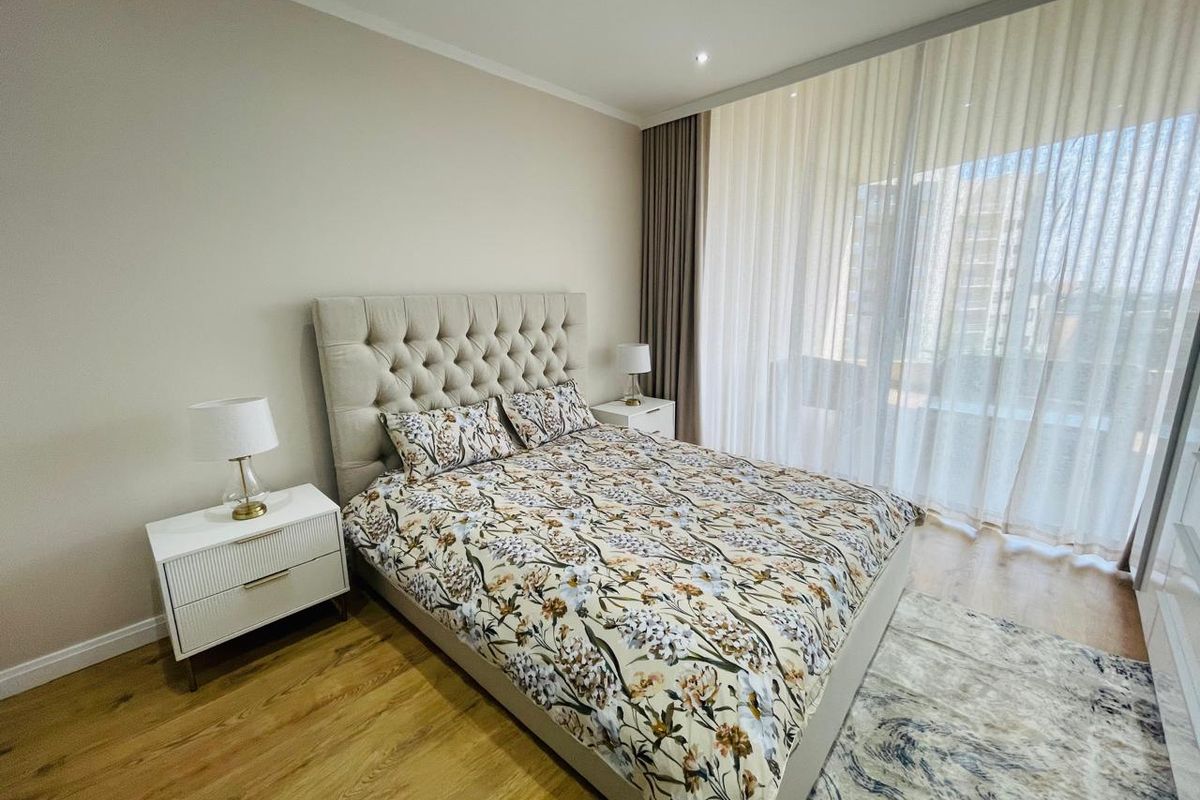 A well-maintained bedroom featuring laminate flooring, recessed downlighting, and floor-to-ceiling curtains providing natural light control.