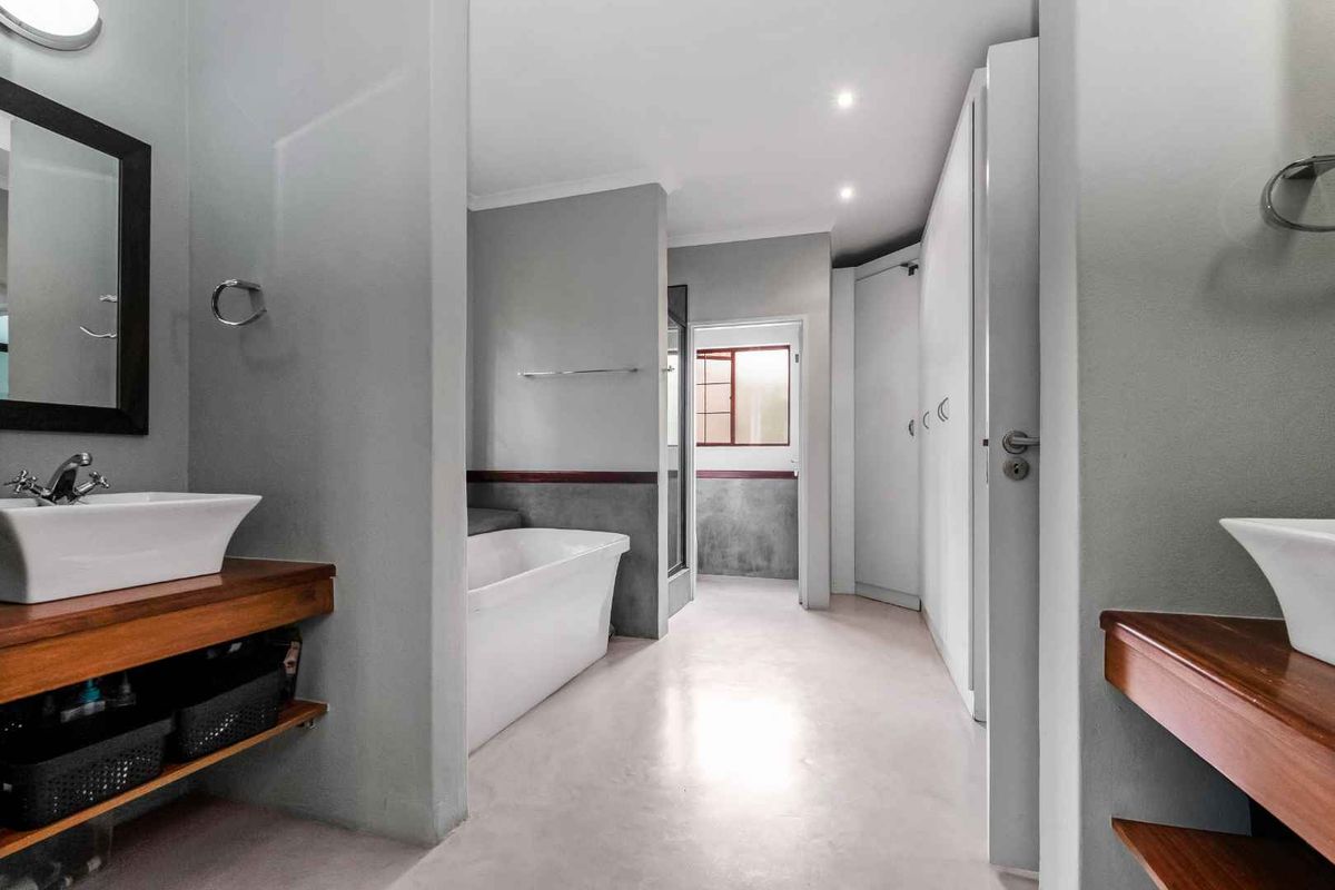 Modern bathroom featuring dual vessel sinks on wooden vanities, a freestanding bathtub, and a separate shower area with polished concrete flooring.