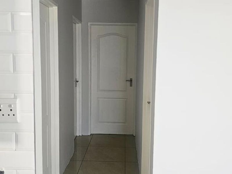A clean, neutral-toned hallway featuring tiled flooring, white internal doors, and classic cove cornice detailing.