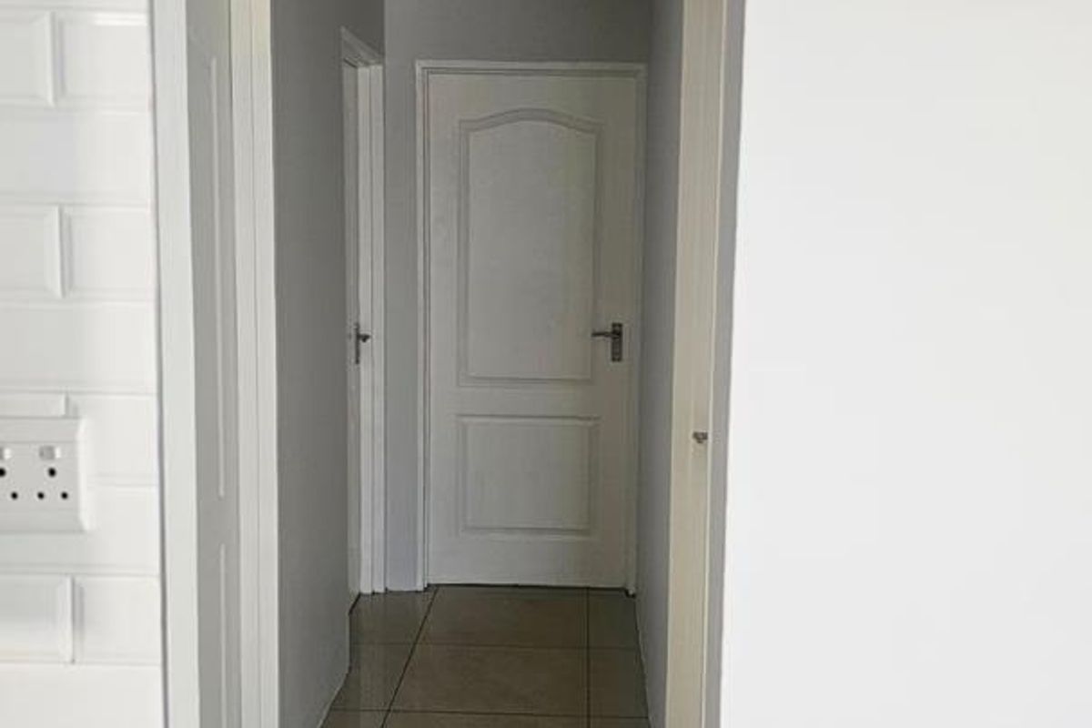 A clean, neutral-toned hallway featuring tiled flooring, white internal doors, and classic cove cornice detailing.