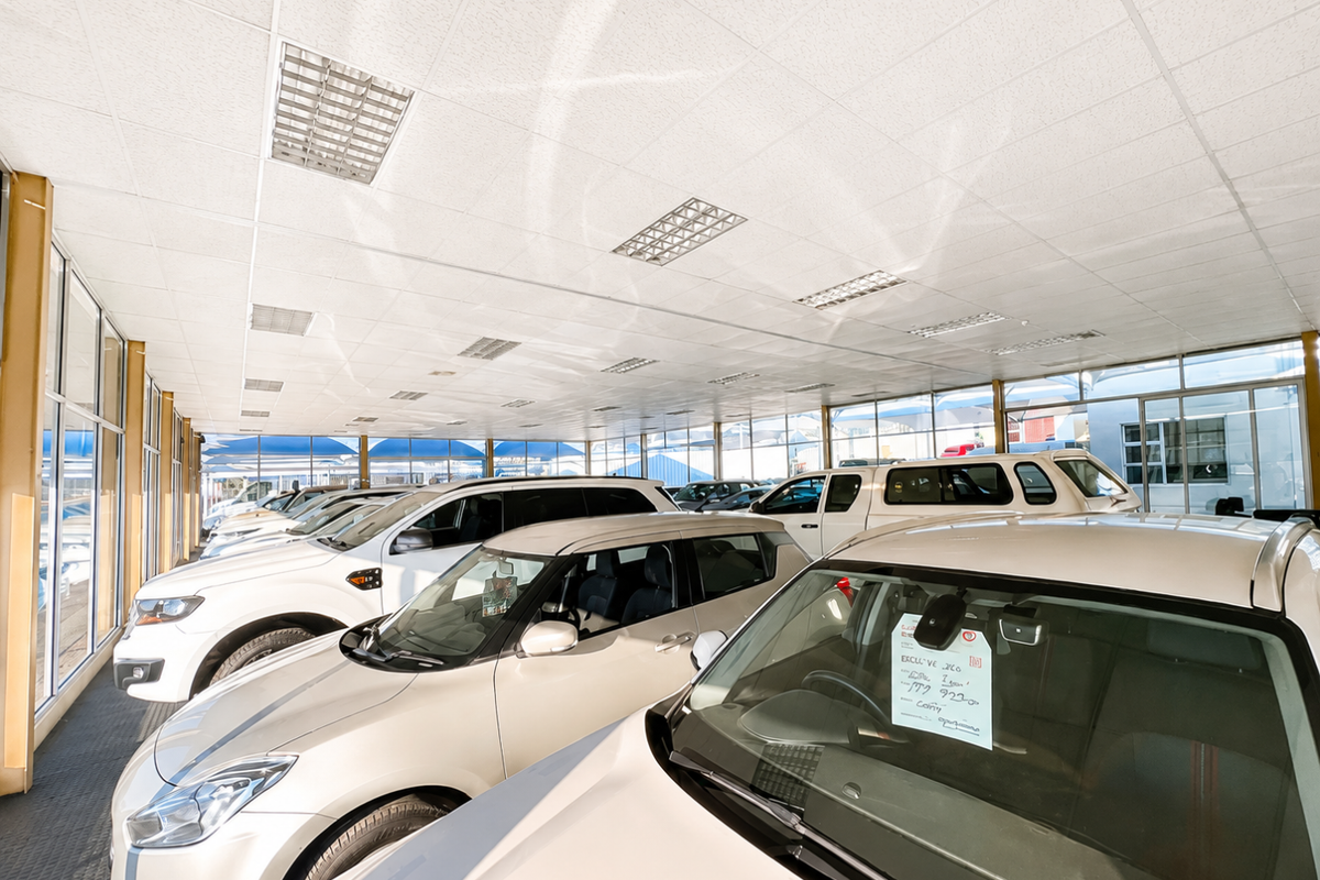 A spacious retail showroom featuring a suspended ceiling with recessed lighting, large glass windows, and durable rubberized flooring, currently utilized for vehicle display.