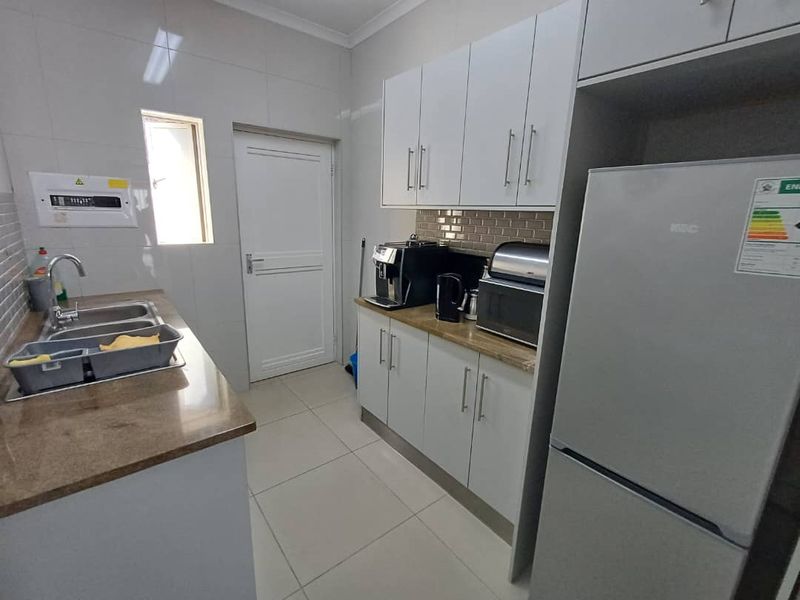 A functional scullery featuring granite countertops, double bowl sink, subway tile backsplash, and ample built-in cabinetry for storage and utility needs.
