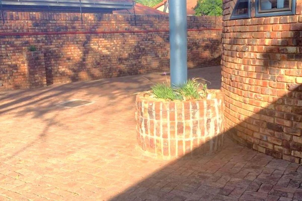 A paved rear courtyard area featuring a curved brick wall, a built-in brick planter, and a metal support column.