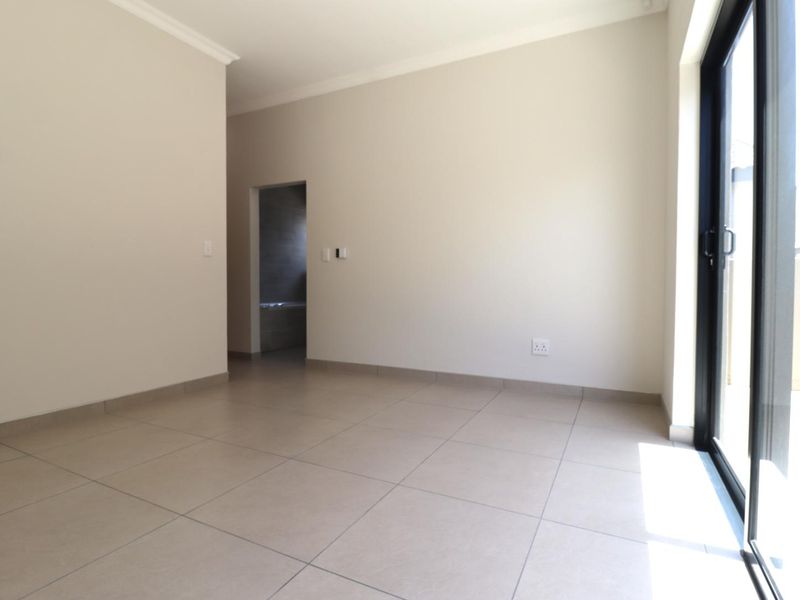 A bright, empty bedroom featuring neutral tiled flooring, coving, and a large sliding glass door providing access to an outdoor area.