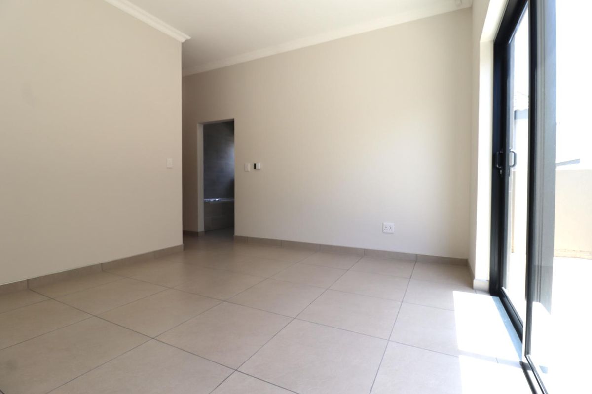 A bright, empty bedroom featuring neutral tiled flooring, coving, and a large sliding glass door providing access to an outdoor area.