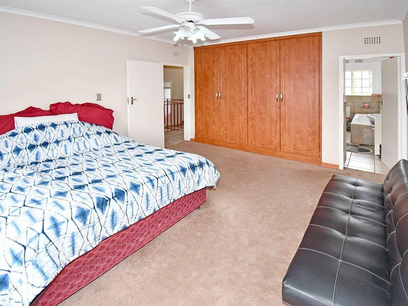 Spacious bedroom featuring built-in wooden cupboards, a ceiling fan, and direct access to an en-suite bathroom.